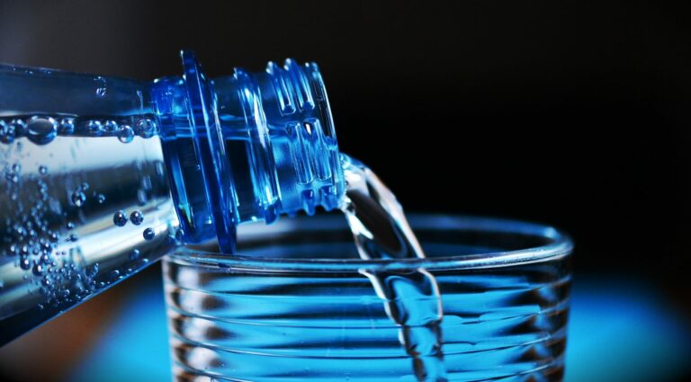 How to Start a Water Company? Water is poured from a blue plastic bottle into a clear glass, highlighting the product of water bottling manufacturers.